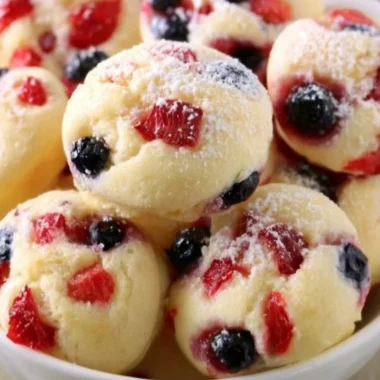 Berry protein pancake bites stacked on a plate, topped with fresh berries.