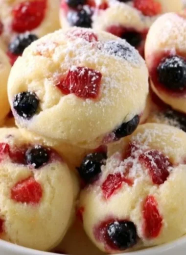 Berry protein pancake bites stacked on a plate, topped with fresh berries.