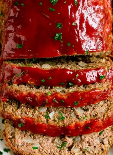 A slice of classic meatloaf on a plate with fresh herbs and side dishes