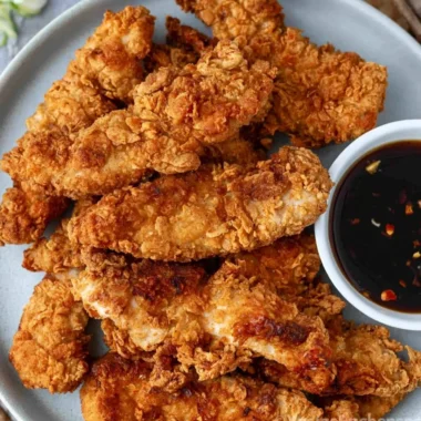 Crispy honey garlic chicken tenders served on a plate with dipping sauce.