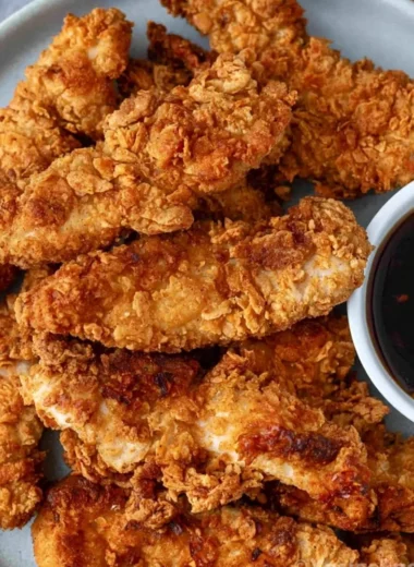 Crispy honey garlic chicken tenders served on a plate with dipping sauce.