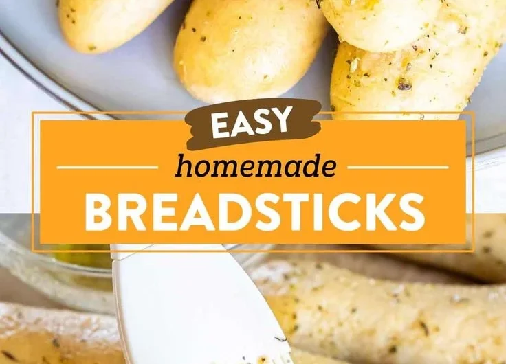 Homemade garlic herb breadsticks on a baking tray with herbs and melted butter.