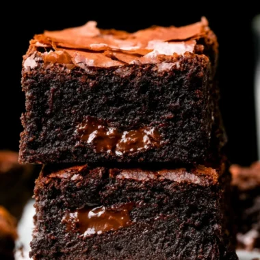 Ultimate fudgy brownies topped with chocolate and served on a rustic plate.