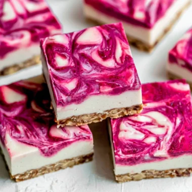 Vegan raspberry cheesecake bars on a plate, topped with fresh raspberries.