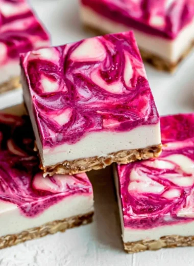 Vegan raspberry cheesecake bars on a plate, topped with fresh raspberries.