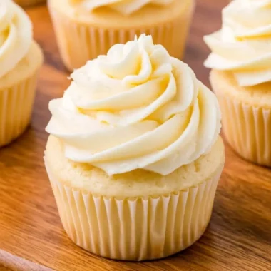 Cozy vanilla cupcakes topped with creamy frosting on a rustic wooden table.