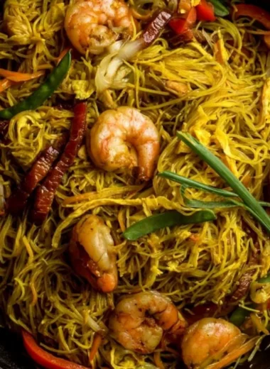 Delicious Singapore Noodles recipe served in a bowl with fresh vegetables.