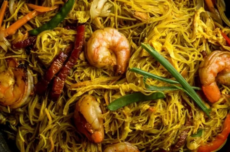 Delicious Singapore Noodles recipe served in a bowl with fresh vegetables.